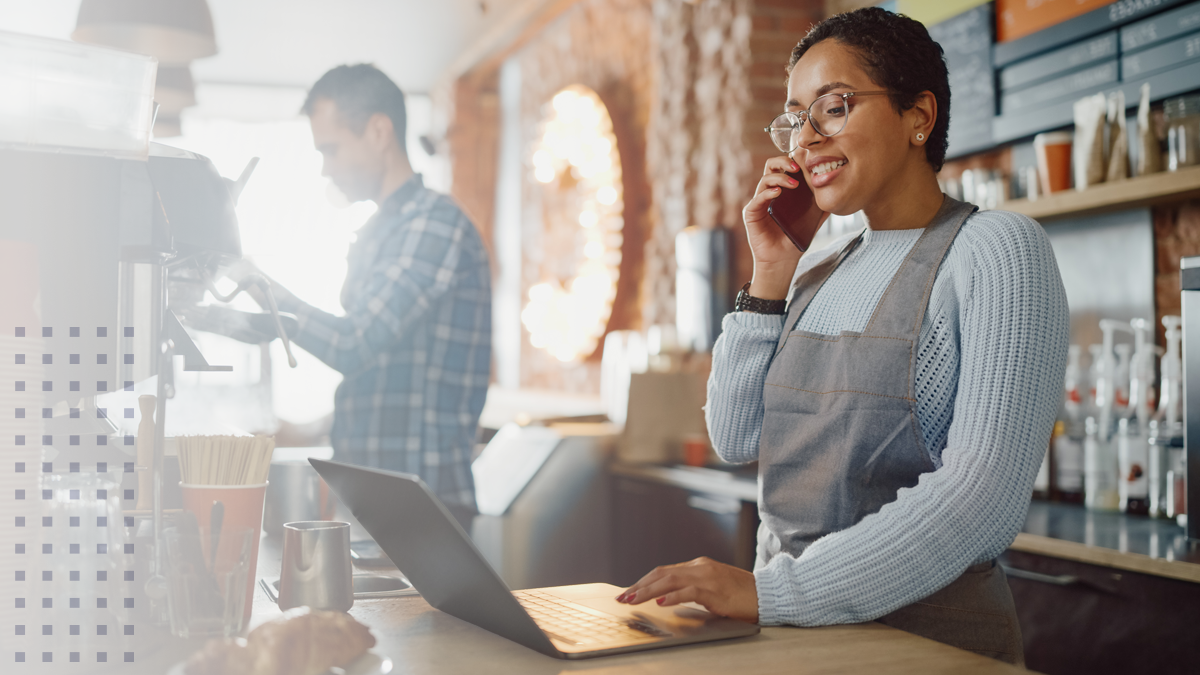 A woman on the phone and laptop while working at a small business coffee shop