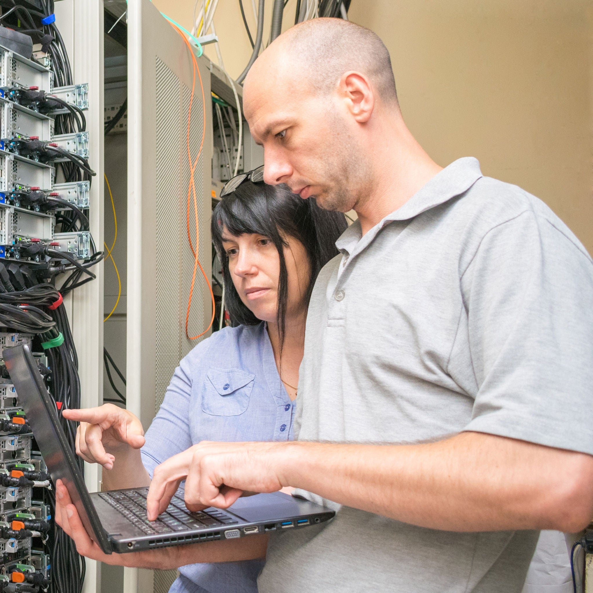 Experts look at the computer screen in the data center. System engineers customize hardware. A man and a woman with a notebook work in a server room. engineers with laptop